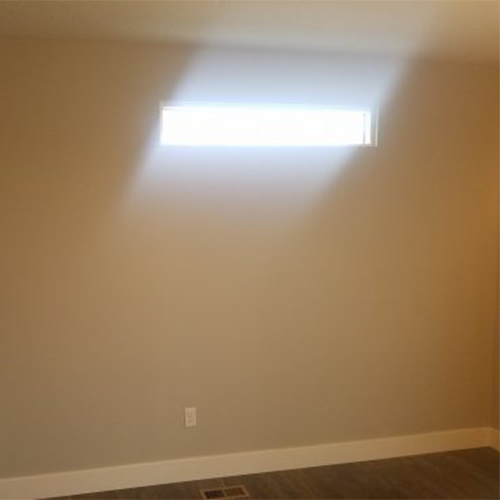 Plain beige wall with a small horizontal window letting in natural light, above a white baseboard.