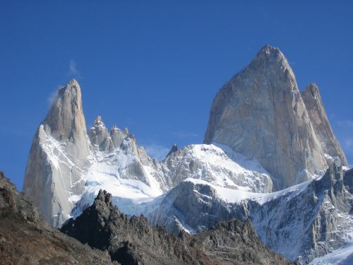 Snow-capped jagged mountain peaks rise sharply into a clear blue sky, with rugged rocky terrain in the foreground—an iconic scene often found near homes in Utah.