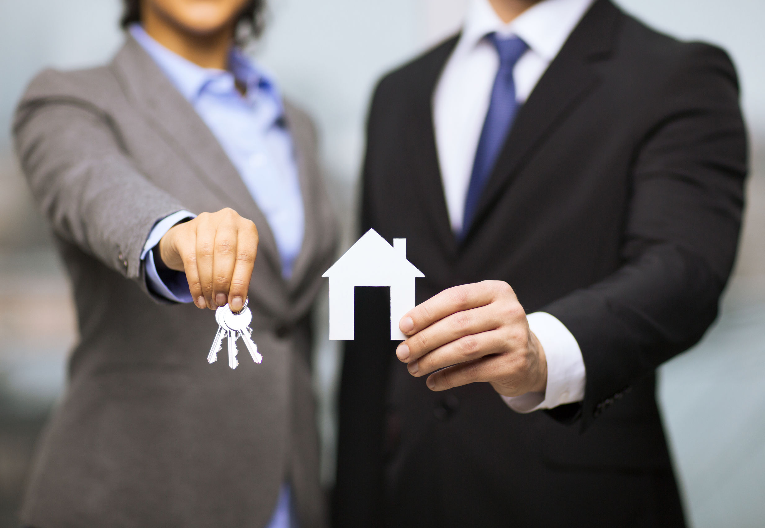 two real estate agents holding keys and house cutout