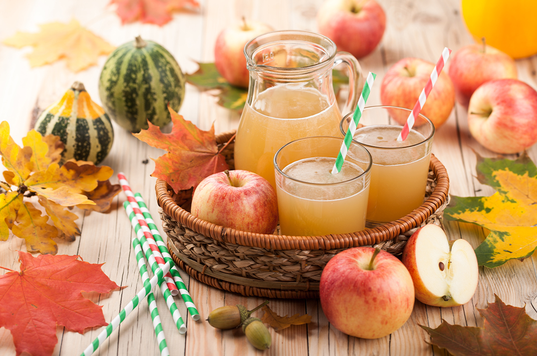 A wicker basket holding two big glasses of apple cider decorated for the fall season..