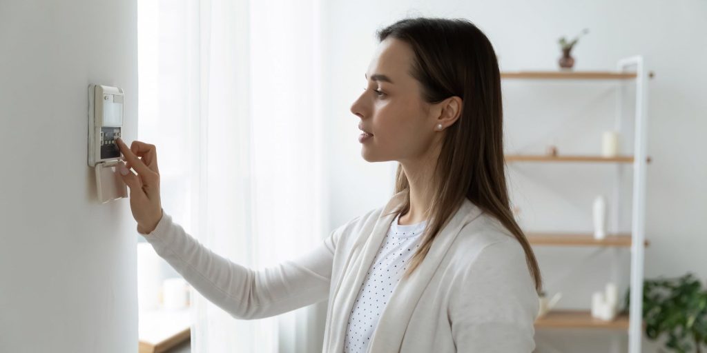 Woman Using Thermostat To Lower Energy Costs At Home