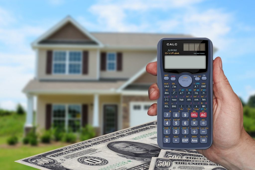 Calculator Held in Front of New Home With Money Below
