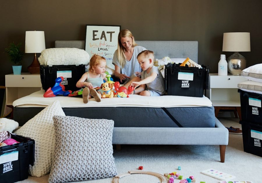 Woman and 2 Children Sitting on Bed Unpacking Boxes in a New Home