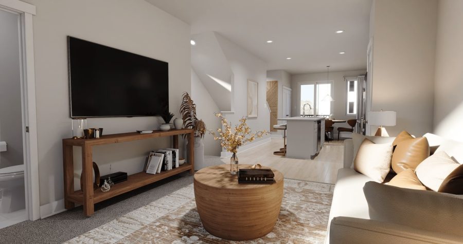 A modern, open-concept living room with a neutral color palette, featuring a wall-mounted TV, a wooden console table with decor, and a round wooden coffee table in the center adorned with a decorative vase and books.