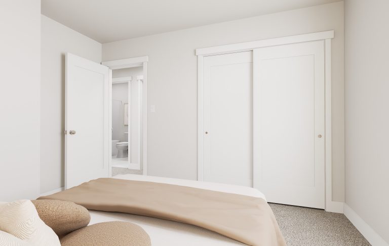 A minimal, modern bedroom with neutral tones—common in many homes in Utah—featuring a neatly made bed, pillows, beige blanket, closed sliding closet doors, and an open door revealing an adjoining bathroom.