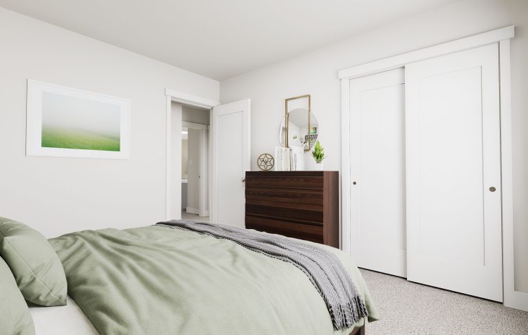 A minimal bedroom in homes in Utah, featuring a neatly made bed with green bedding, a dark wooden dresser adorned with decor and a mirror, white sliding closet doors, and a framed landscape photo on a light-colored wall.