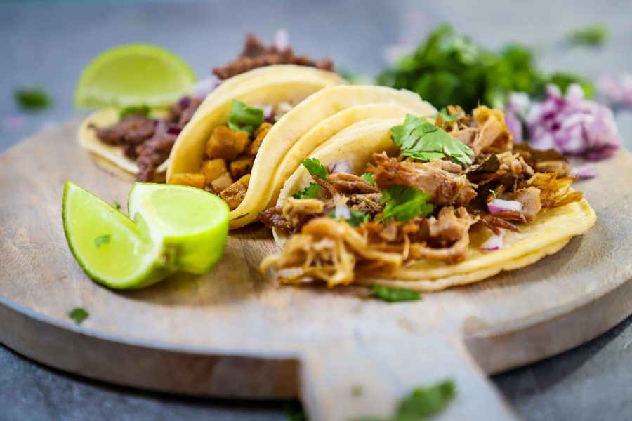 A close-up of tacos filled with fresh vegetables, meat, and topped with herbs, served on a wooden platter with lime wedges.