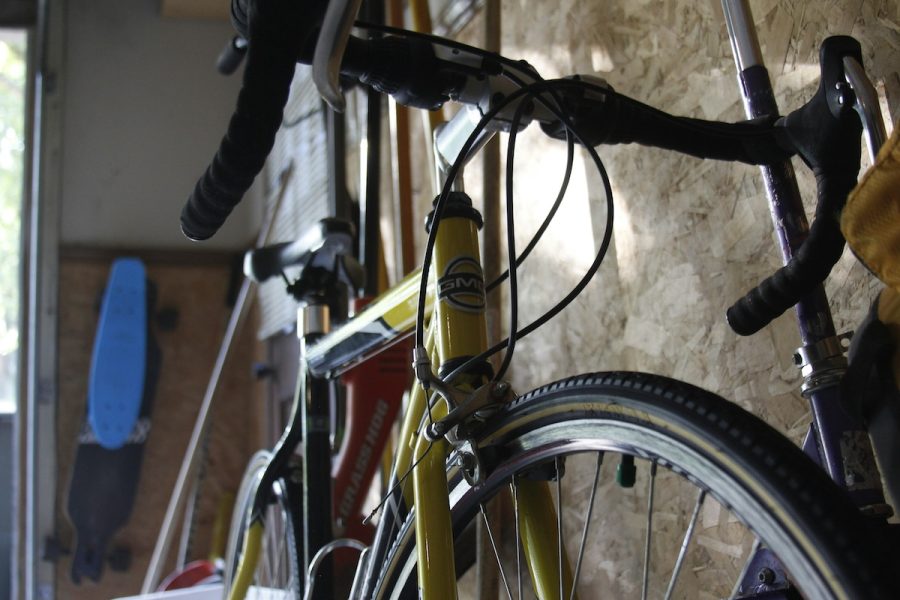 Close-up of a yellow road bike with drop handlebars in a garage, surrounded by other bicycles and a blue longboard. Indoor storage space with cycling and sports equipment.