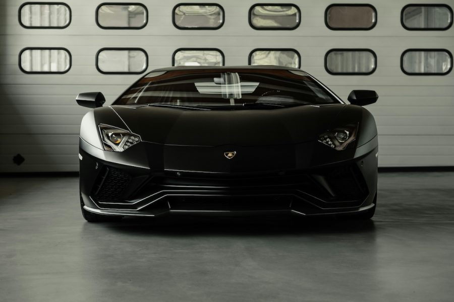 Matte black Lamborghini sports car parked in a garage with a modern industrial design. Luxury high-performance vehicle with sleek aerodynamic design and aggressive front fascia.