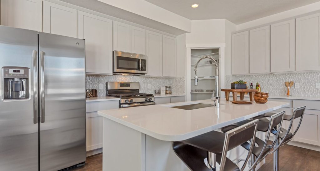 Modern kitchen with white cabinets, stainless steel appliances, gas stove, microwave, and a large island with a sink and three bar stools—perfectly designed like many stylish homes in Utah. Decor and kitchen items add charm to the spacious counters.