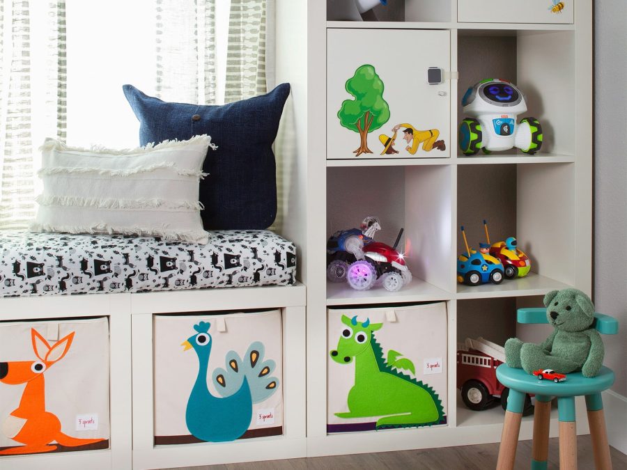 Colorful children's playroom with built-in white cubby storage, featuring animal-themed fabric bins, toy vehicles, plush toys, and a cushioned bench by the window.