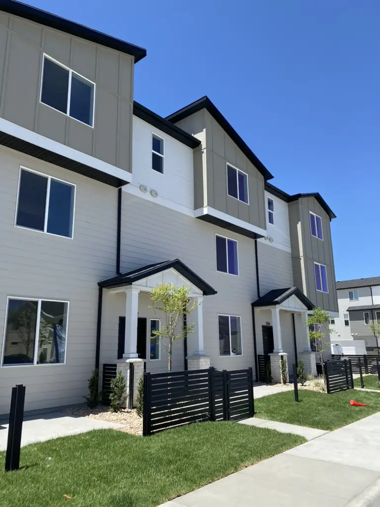 Row of new three-story townhomes with gray siding, white trim, and black fences along a walkway