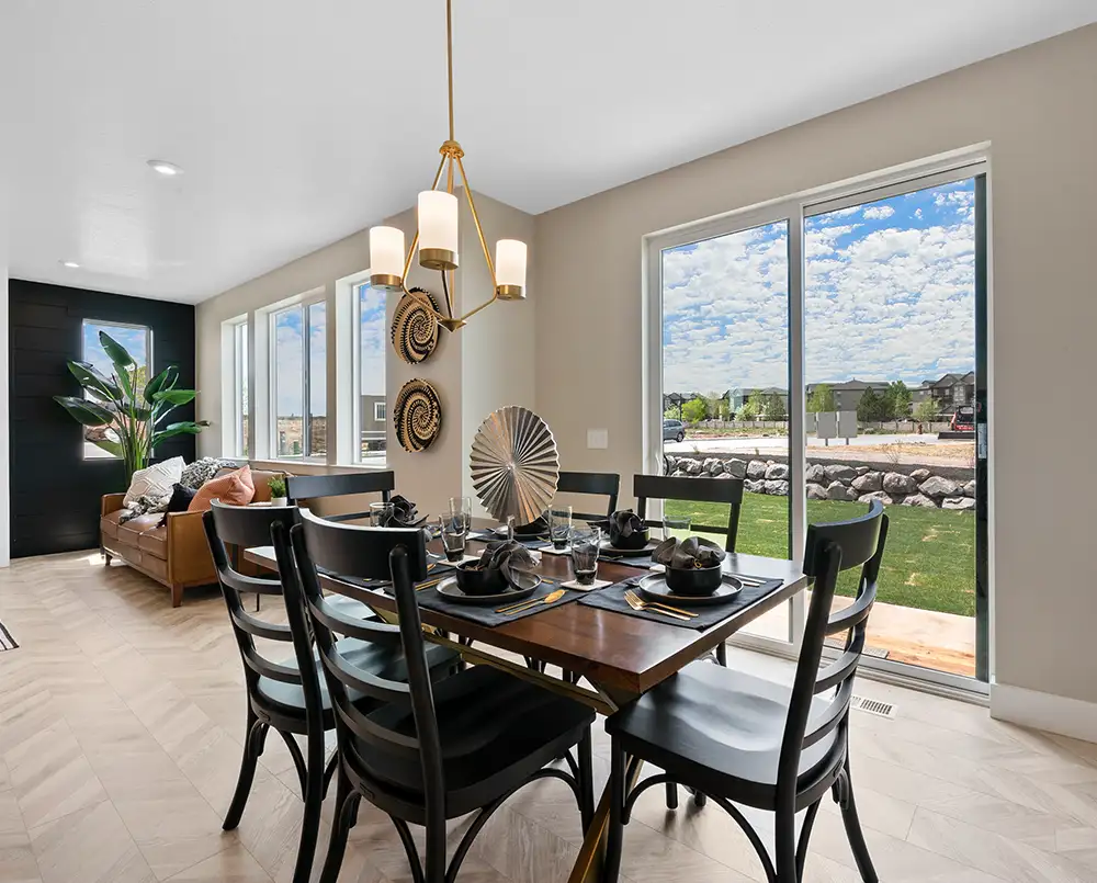 Dining room with wood table set for six, black chairs, gold chandelier, woven wall plates, and sliding glass doors to a yard.