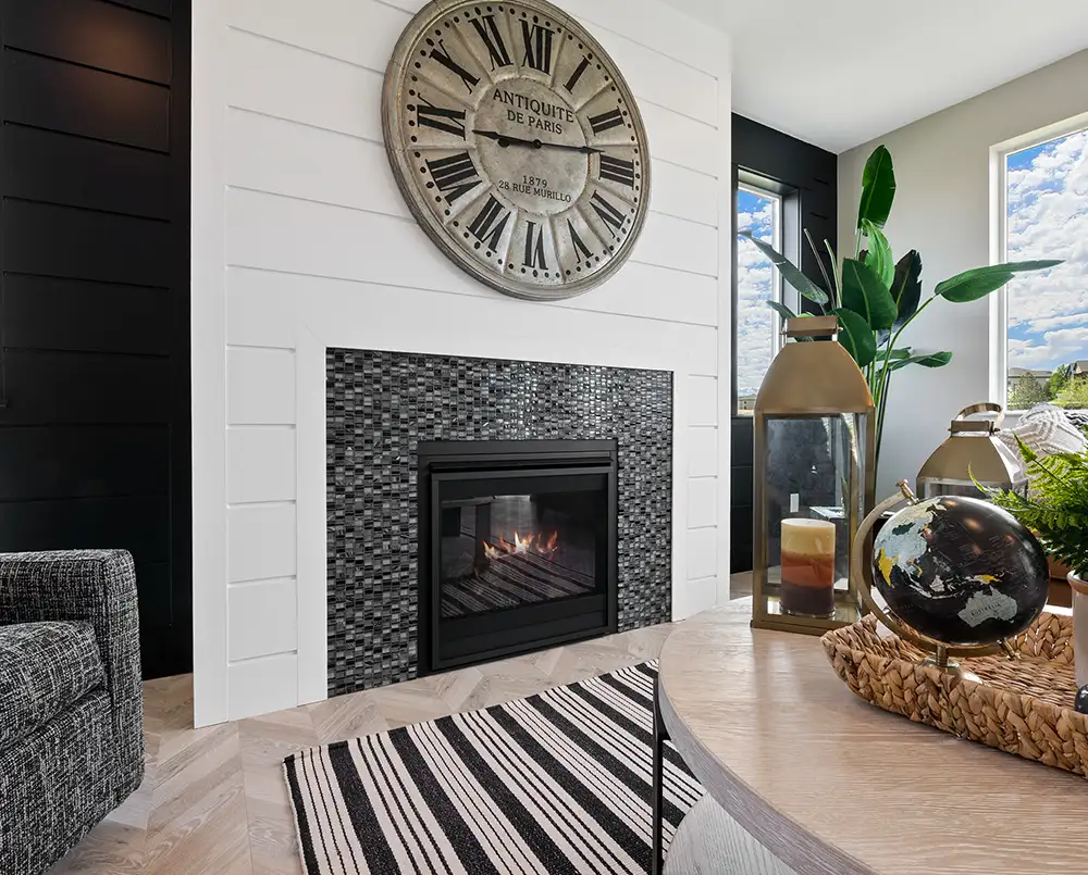Fireplace with mosaic tile surround on a white shiplap wall, oversized Roman numeral clock, lantern, globe, and striped rug.