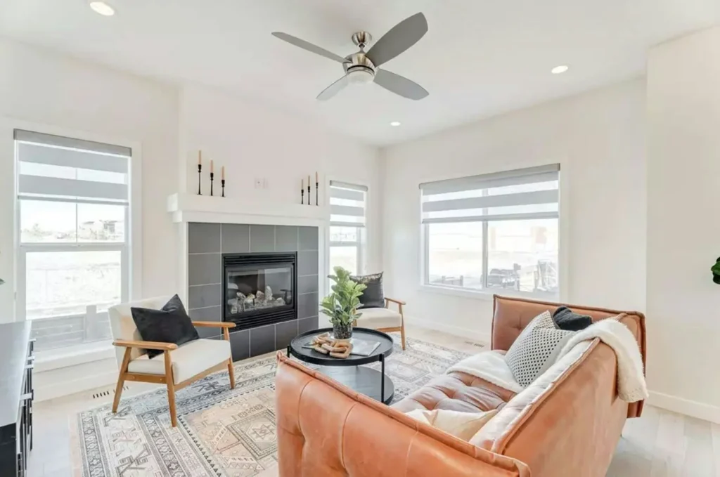 Modern farmhouse living room with gabled gas fireplace, black tile surround, cognac leather sofa, and large black-frame windows.