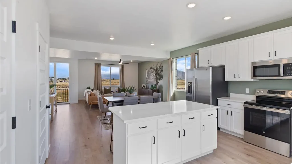 Open-concept kitchen with white cabinets and island, sage accent wall, opening to a dining and living area with mountain views.