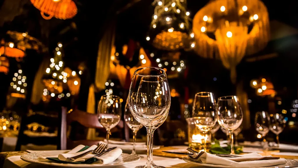 Upscale restaurant table set with crystal wine glasses and white linens, with warm chandelier lighting and bokeh in the background.