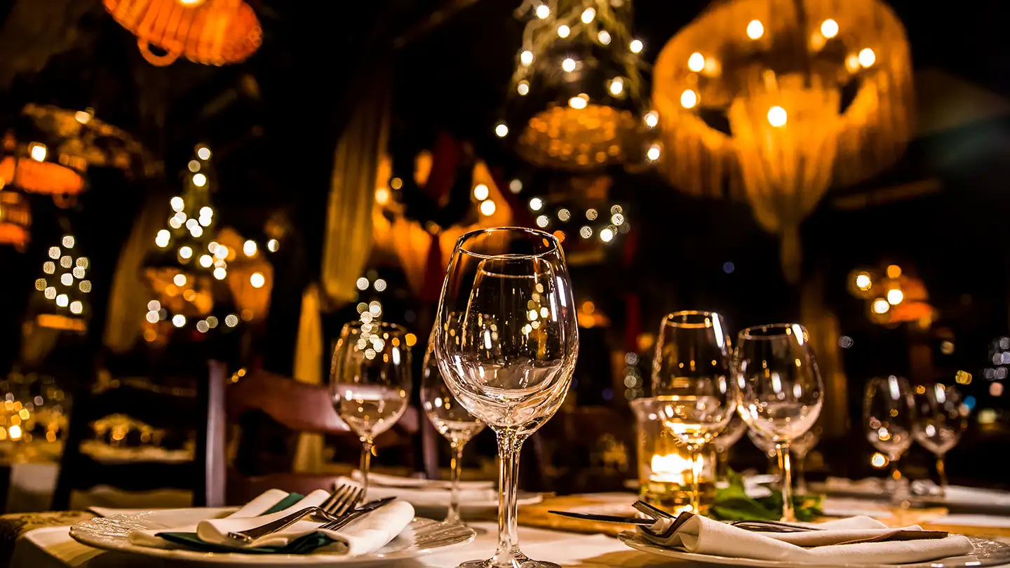 Upscale restaurant table set with crystal wine glasses and white linens, with warm chandelier lighting and bokeh in the background.