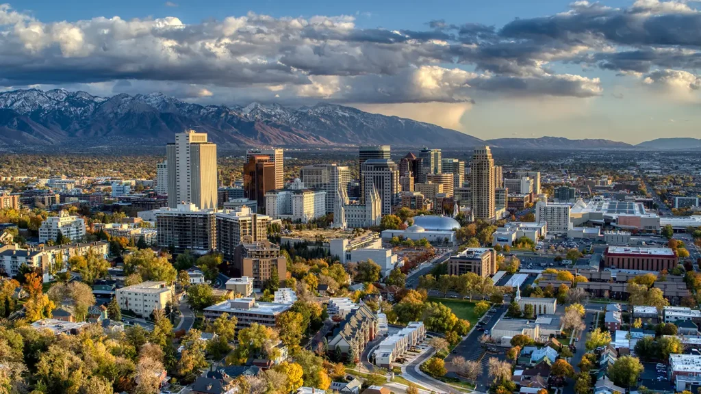 Aerial view of downtown Salt Lake City’s skyline with high-rises and the snow-tipped Wasatch Mountains behind at golden hour.