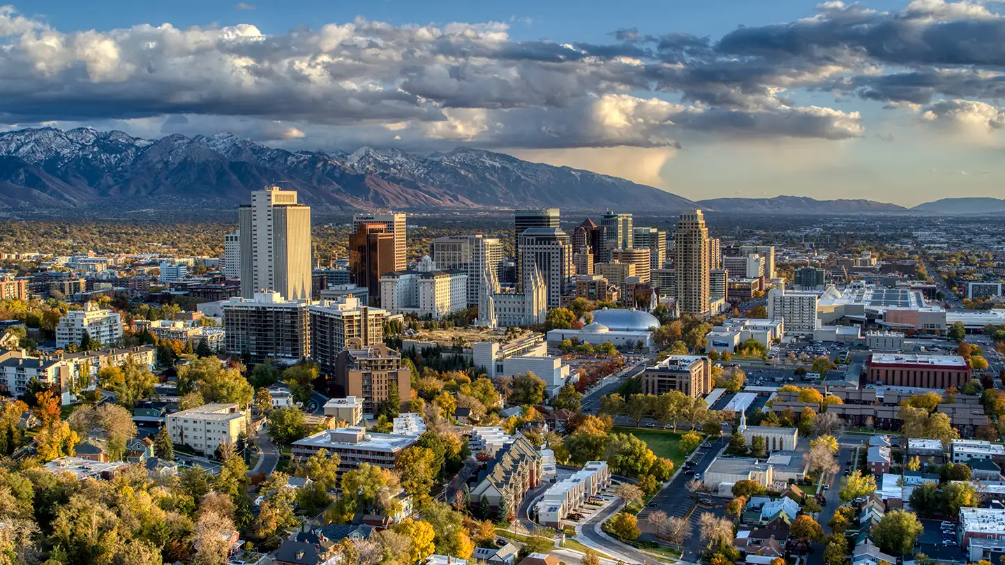 Aerial view of downtown Salt Lake City’s skyline with high-rises and the snow-tipped Wasatch Mountains behind at golden hour.