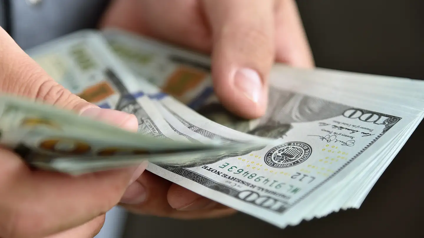 Close-up of two pairs of hands exchanging a stack of U.S. one-hundred-dollar bills.
