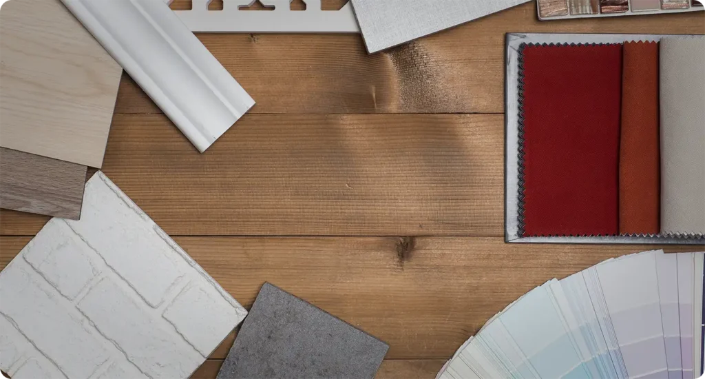 Flat lay of home design samples including wood, painted brick, tile, fabric swatches, and a paint fan deck on rustic wood planks.
