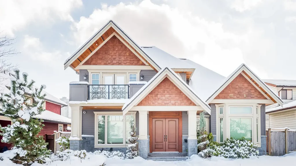 Craftsman-style two-story home with snow-covered roof and yard, wooden double front doors, and multiple gabled rooflines.