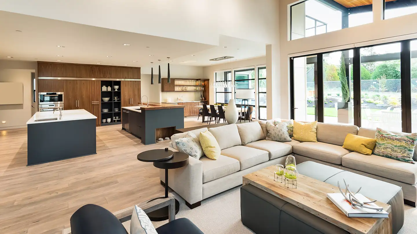 Open-concept great room with a sectional sofa, two-island kitchen, dining area, and floor-to-ceiling glass doors to the yard.
