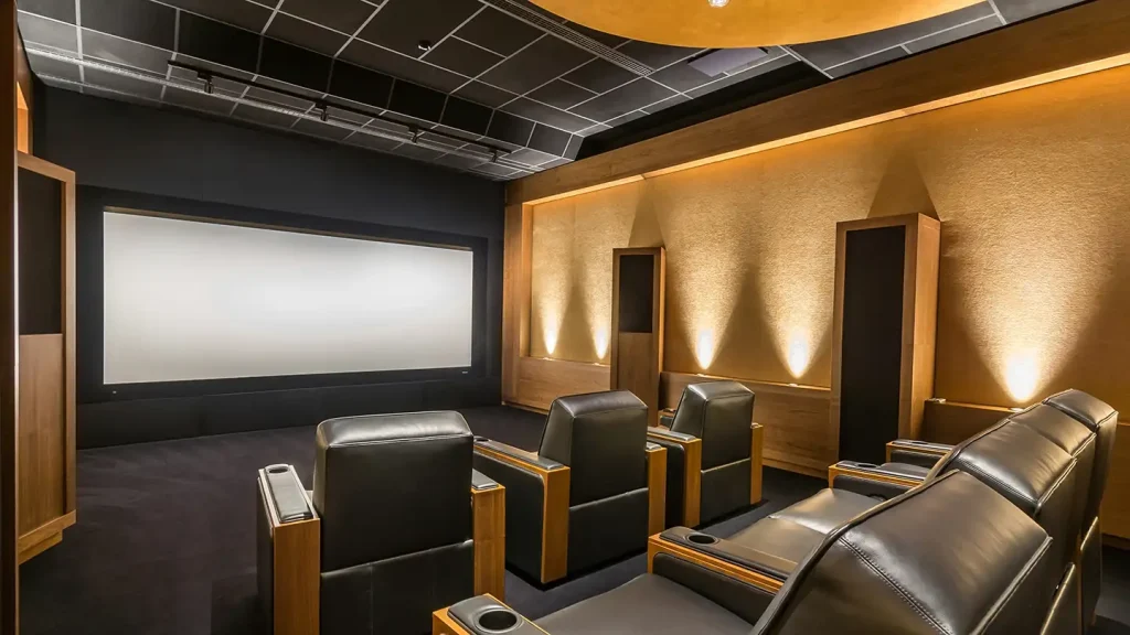 Home theater room with a large projection screen, tiered black leather recliners, wood-paneled walls, and warm accent lighting.