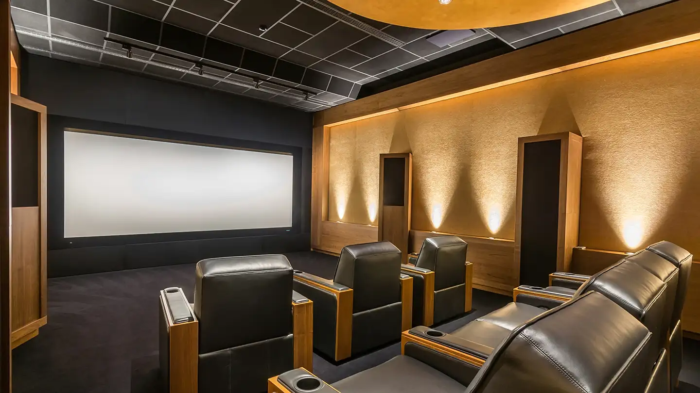 Home theater room with a large projection screen, tiered black leather recliners, wood-paneled walls, and warm accent lighting.