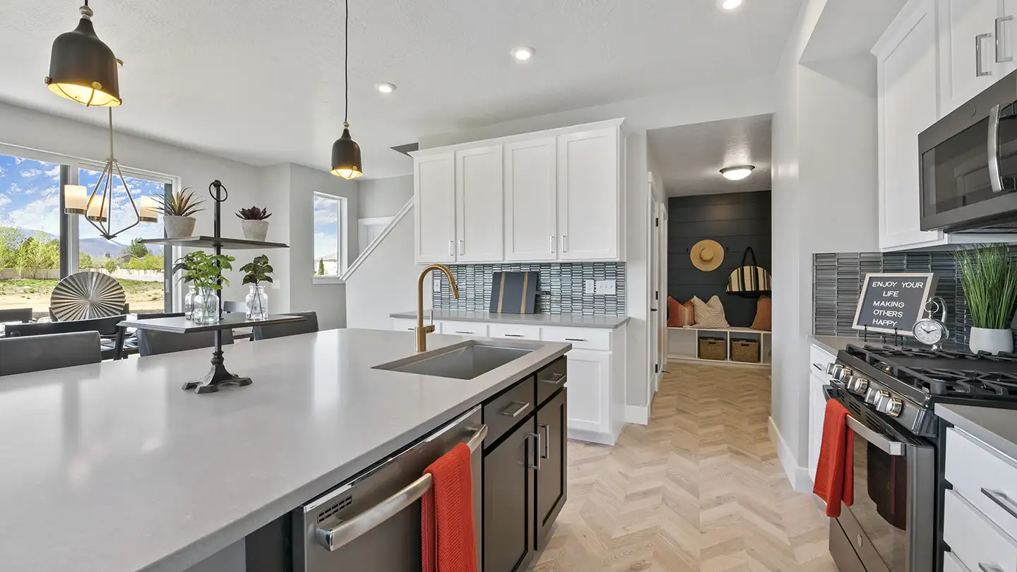 Modern kitchen with herringbone laminate flooring, white cabinets, gray island sink, gas range, and a mudroom view beyond.