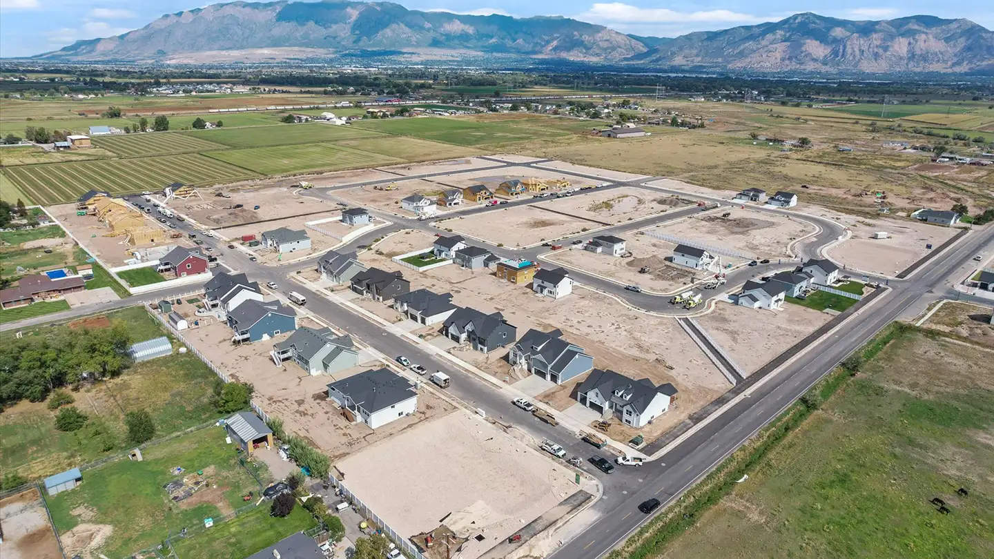 Aerial view of a developing residential neighborhood with new houses under construction and mountains in the background.