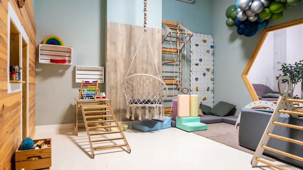 Kids playroom with a climbing wall, wooden ladder, macrame hanging swing, abacus, foam blocks, and balloon garland.