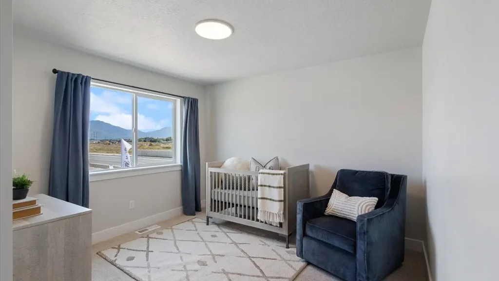Nursery with a wooden crib, navy blue armchair, dresser, blue curtains, and a large window framing distant mountain views.