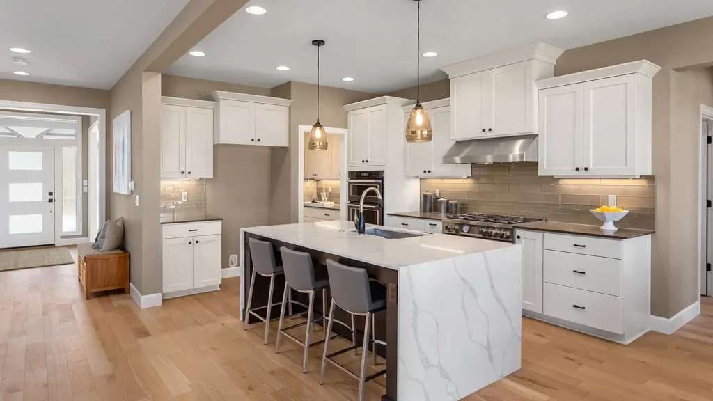 Modern kitchen with white shaker cabinets, a marble waterfall island with three gray bar stools, pendant lights, and hardwood floors.