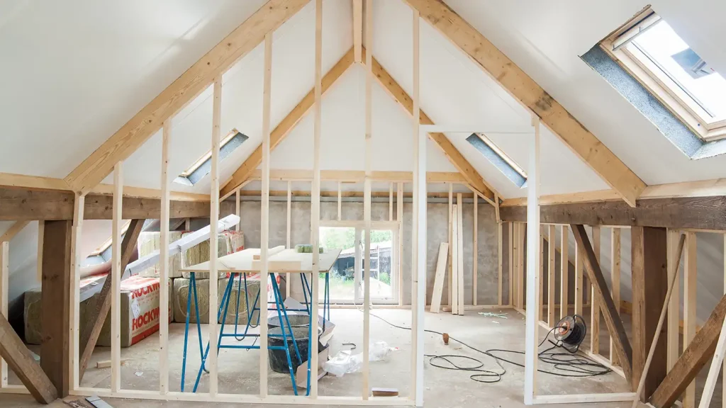 Unfinished attic loft with exposed wood rafters, skylights, insulation panels, and a vaulted ceiling with a window at the end.