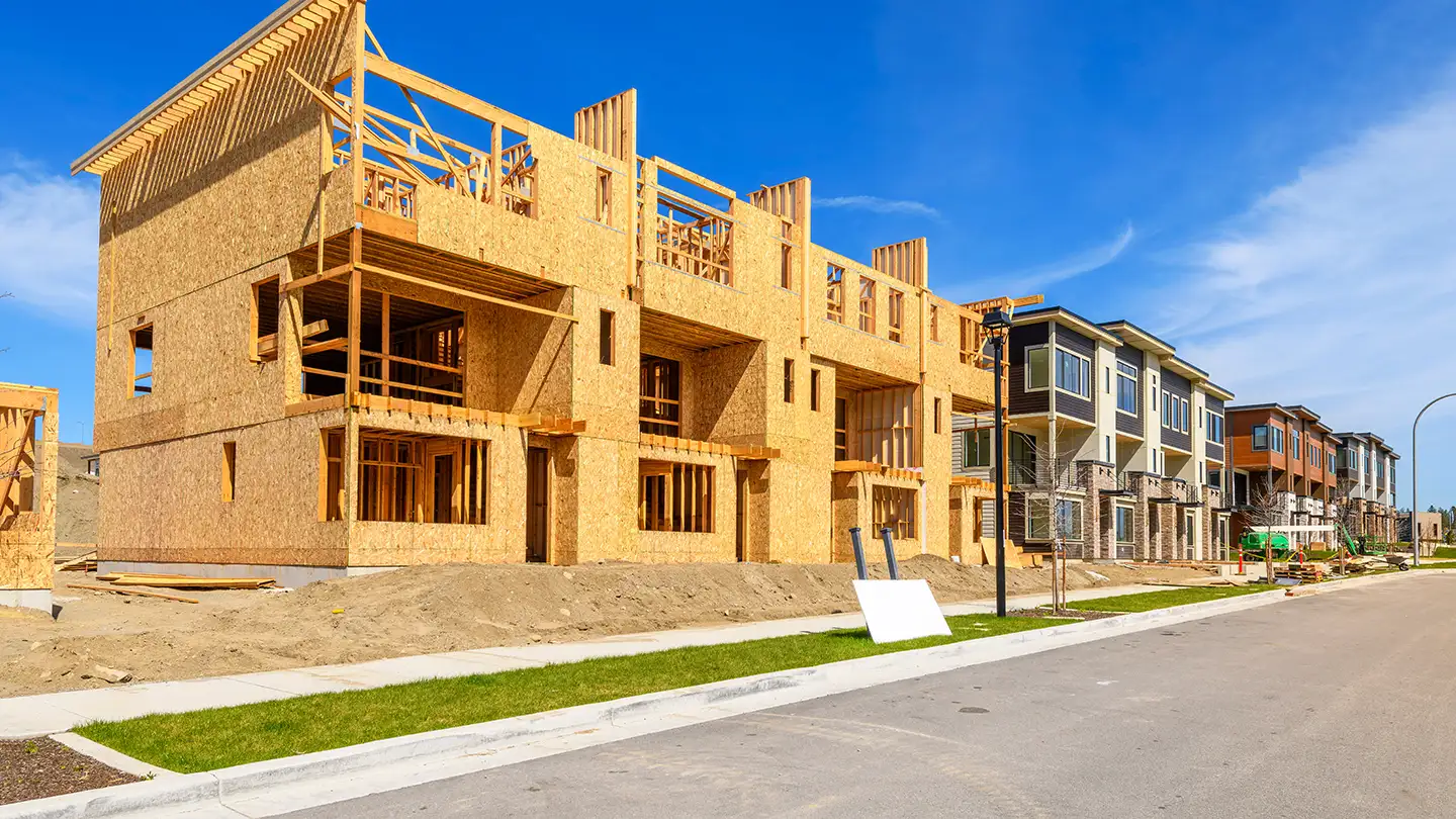 Multi-story townhomes mid-construction with exposed wood framing and OSB wall sheathing under a bright blue sky.