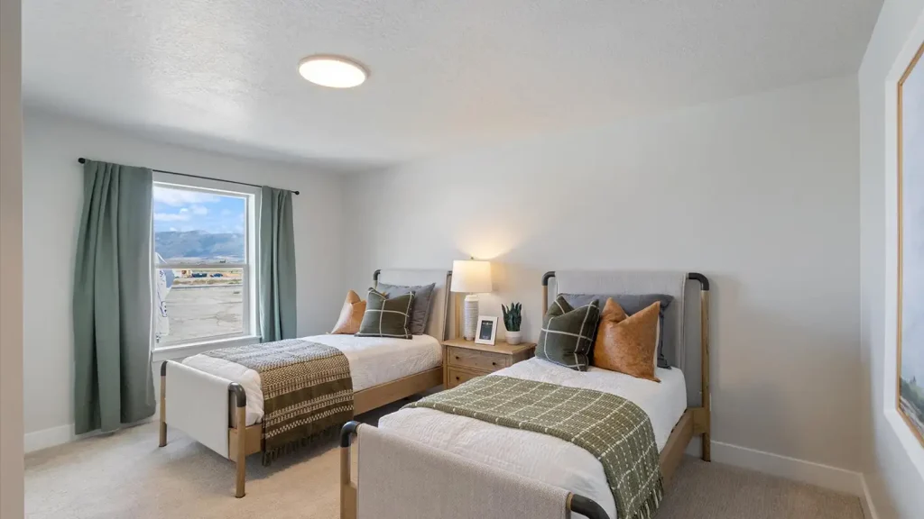 Twin bedroom with two beds dressed in white linens, gray and tan accent pillows, green throws, and a window with mountain views.