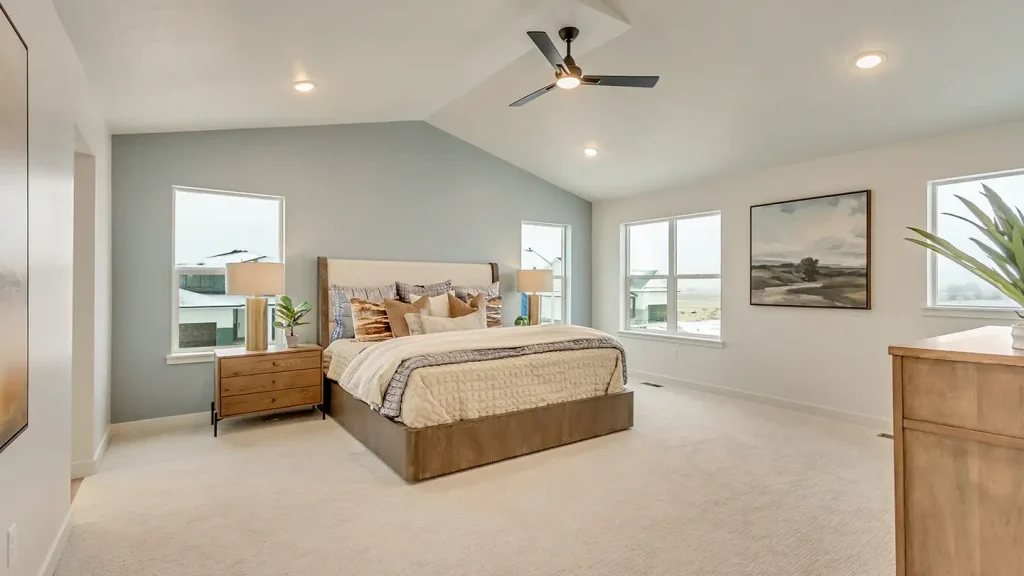 Master bedroom with a king-size bed, sage walls, vaulted ceiling, ceiling fan, large windows, and framed landscape art.