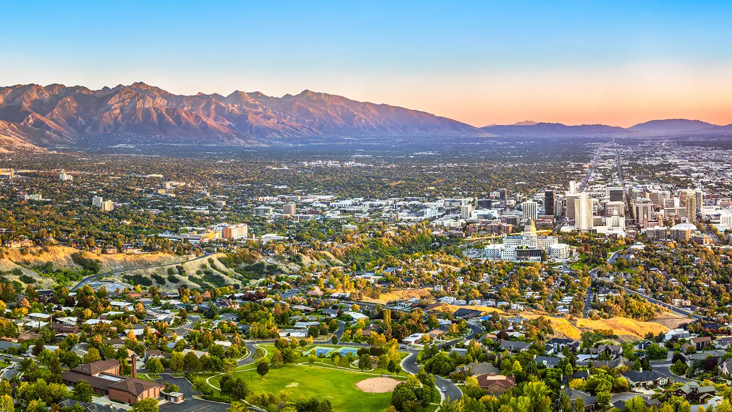 Aerial view of Salt Lake City at golden hour with the Wasatch Mountains, downtown buildings, neighborhoods, and a baseball field.