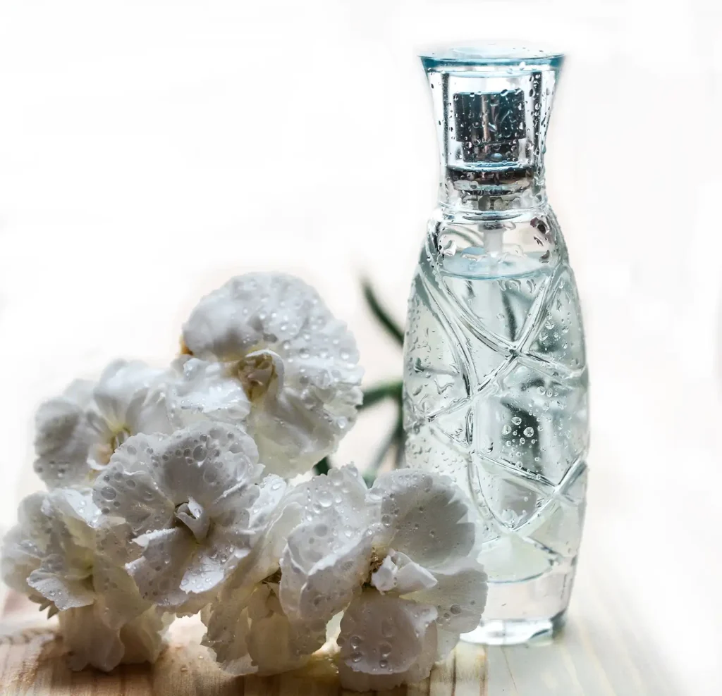 Clear cut-glass perfume bottle beside dewy white carnations on a wood surface, illustrating how scent helps sell a home.