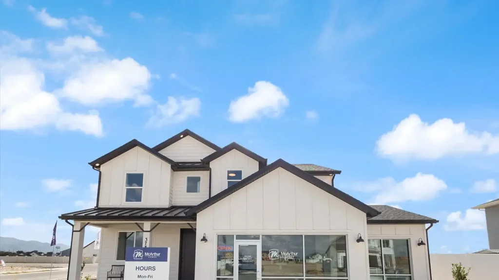 White two-story McArthur Homes model home with multiple gables and an attached sales office under a bright blue sky.