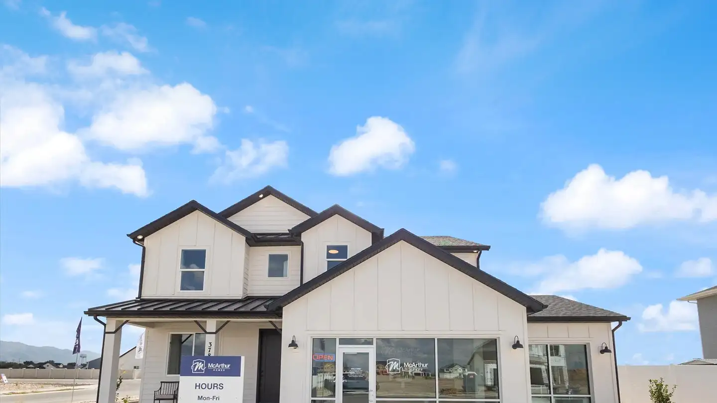 White two-story McArthur Homes model home with multiple gables and an attached sales office under a bright blue sky.