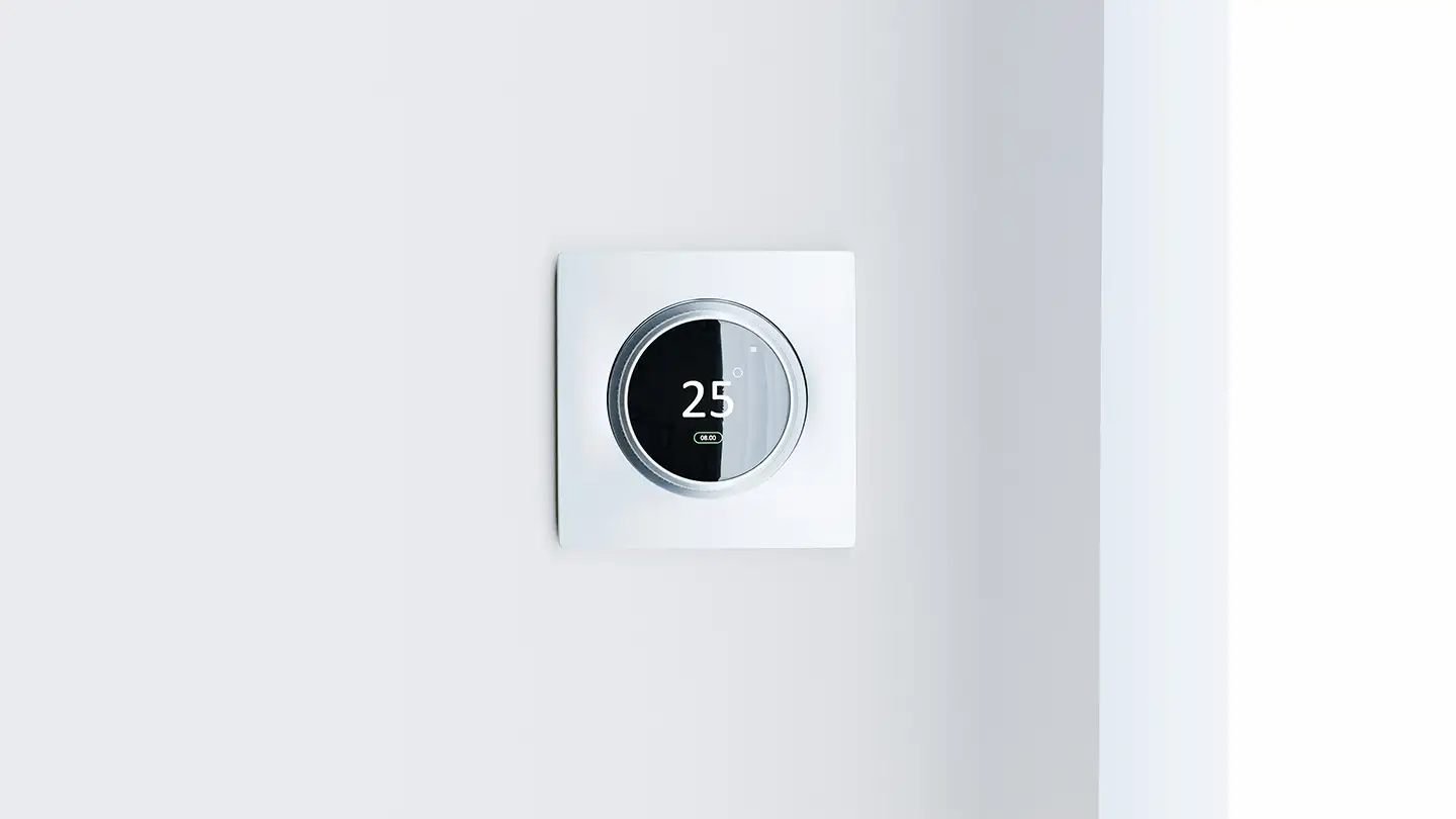 Round smart thermostat mounted on a white wall displaying 25 degrees, an energy-saving feature found in modern new construction homes.