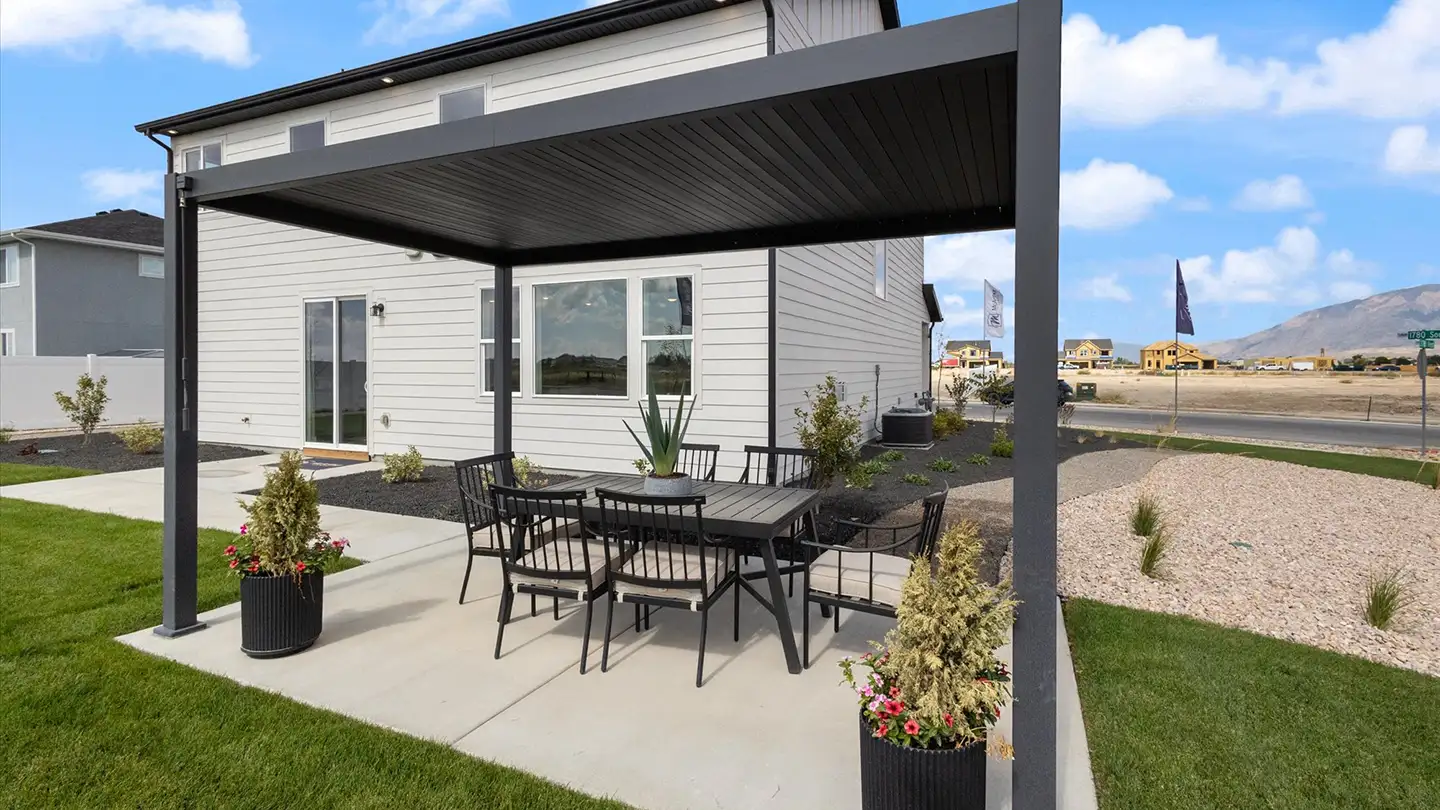 Backyard patio with a black metal pergola, dining table for six, potted flowers, and a white McArthur home behind.