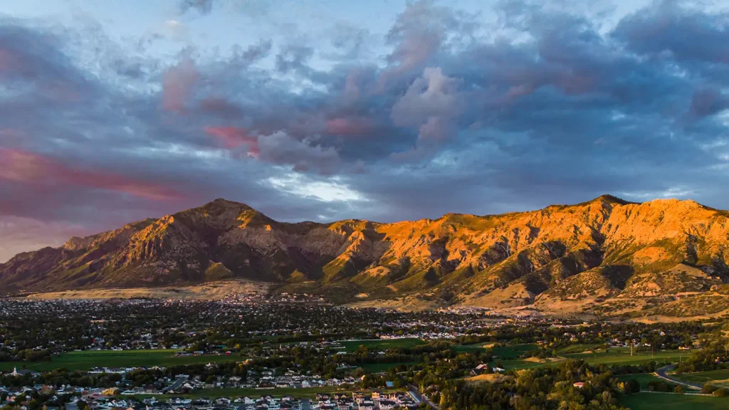 Dramatic sunset over Weber County with golden light on the Wasatch peaks, sweeping clouds overhead, and homes nestled below.