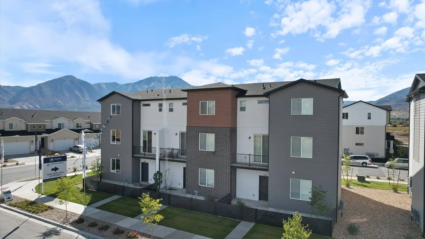 Row of three-story McArthur Homes townhomes with mixed siding, mountains behind, and an Arrowhead community sales sign.