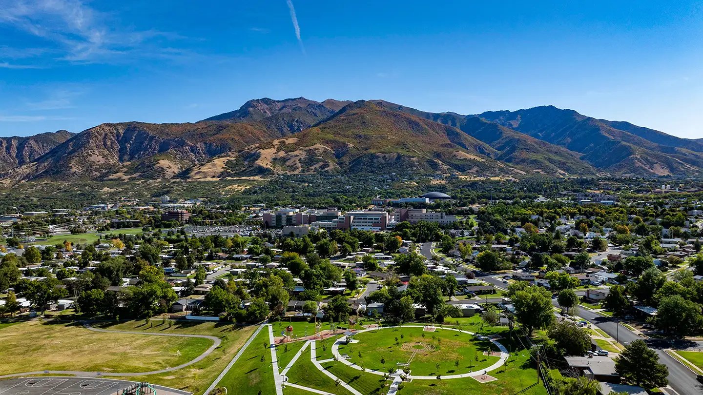 Aerial view of a Utah town with a green park in the foreground, sprawling neighborhoods, and tall mountains in the background.