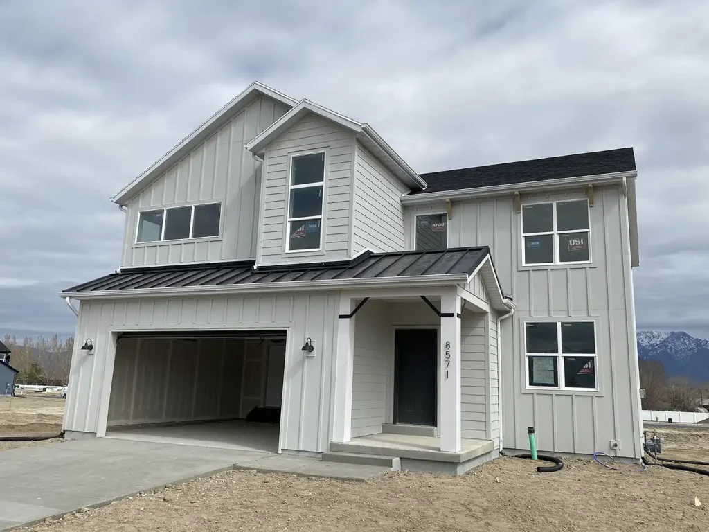 New construction modern farmhouse with light board-and-batten siding, black metal porch roof, two-car garage, address 8571, mountain view behind.