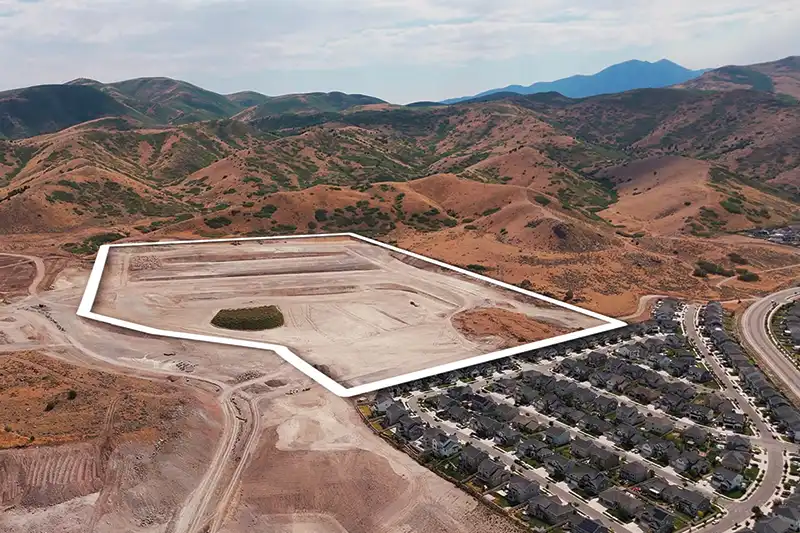 Aerial view of a graded land parcel outlined in white, bordered by homes and foothills